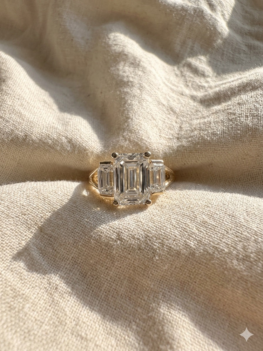 Gold ring with emerald-cut diamonds on a beige fabric background