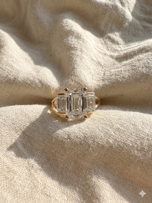 Gold ring with emerald-cut diamonds on a beige fabric background