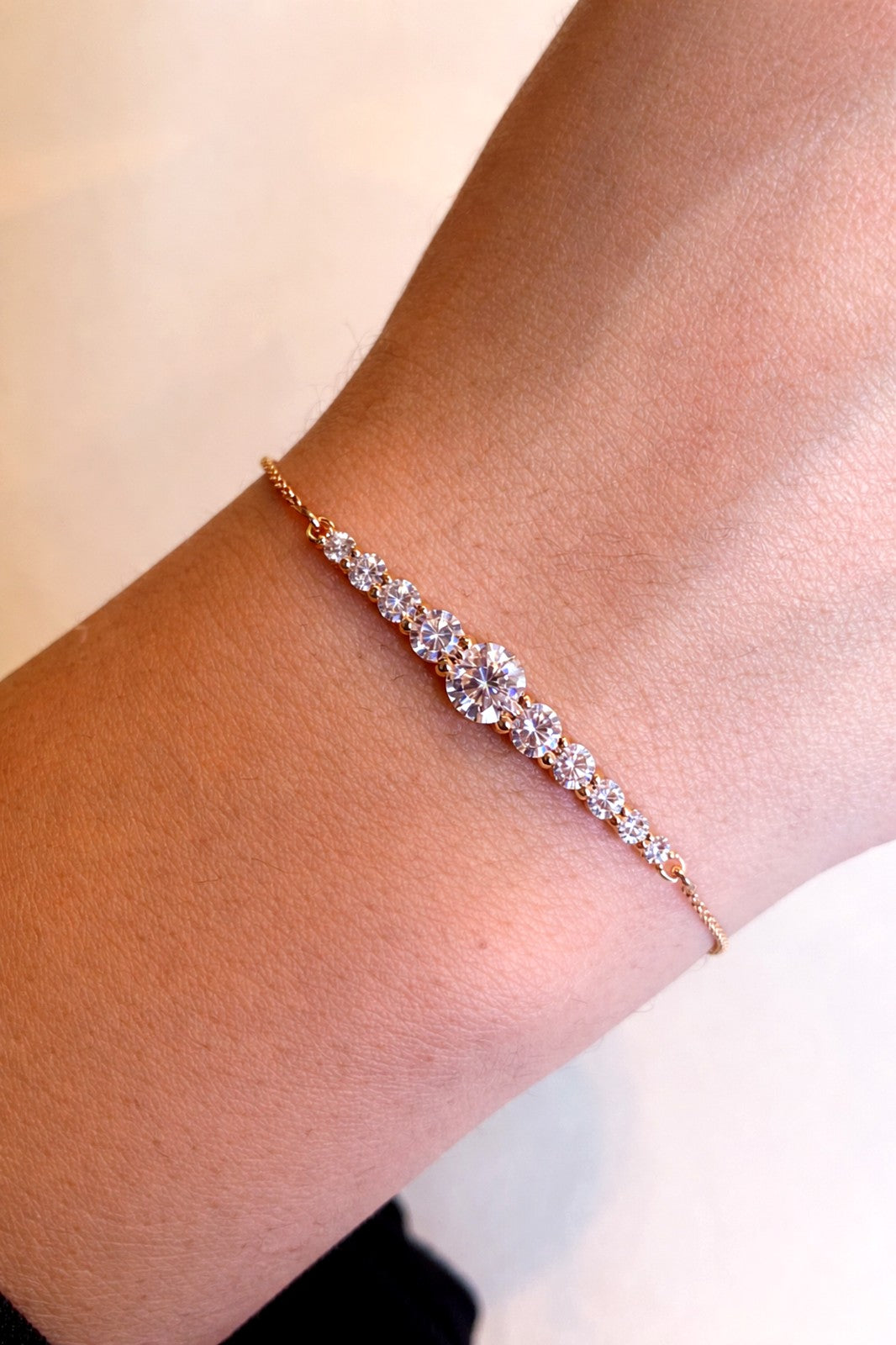 Rose gold bracelet with clear stones on a wrist against a light background